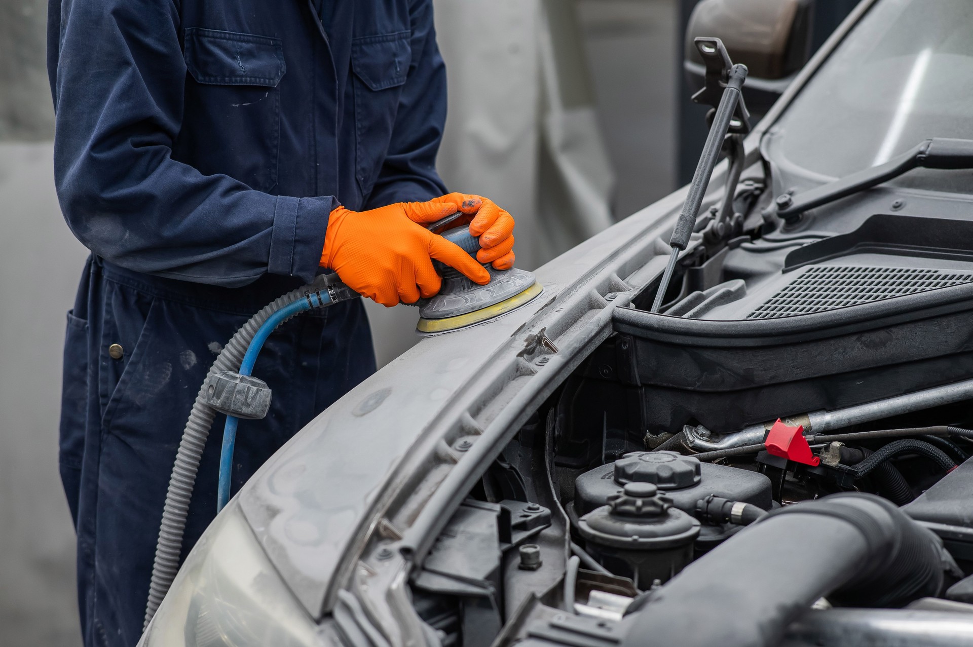 A mechanic sands the putty on a car body with a machine. Repair after an accident.